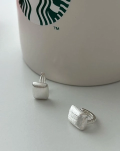 Detail of 925 sterling silver square stud earrings with brushed matte finish on a white cup