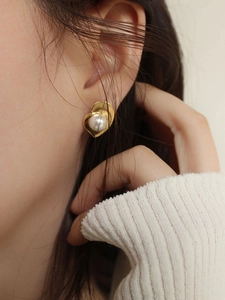 Close-up of elegant gold heart pearl earrings on model with retro metallic texture