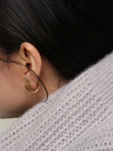 Orecchino a cerchio a spirale dorata in argento 925 indossato da una modella in un maglione