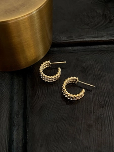 Macro detail of gold-plated twisted rope earrings with high-polish metallic texture