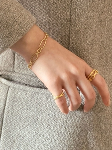 Golden chain bracelet and textured rings set against a grey tweed suit background