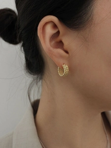 Close-up of a model wearing a gold twisted rope C-shaped hoop earring with vintage texture