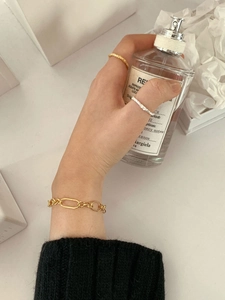 Close-up of gold chain bracelet and hammered rings held with a luxury bottle