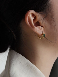 Close-up of model wearing gold hoop earrings with square emerald green gemstone insets