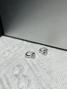Detailed view of silver hoop earrings with cat-shaped zircon studs on white fabric