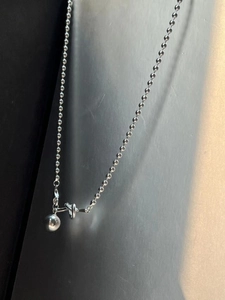 Détail du collier en chaîne à billes argentée avec pendentif sphérique et nœud design