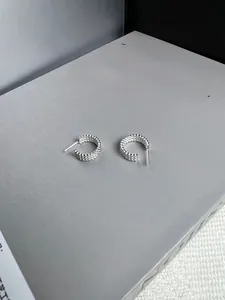 Detailed close-up of 925 silver C-shape twisted hoop earrings on a fashion book background