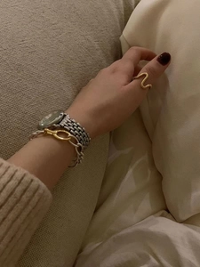 Close-up of a wavy gold ring styled with a chunky link bracelet and a mesh watch
