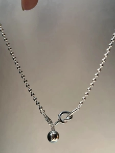 Détail du collier à billes argenté avec fermoir à nœud et pendentif boule en métal poli