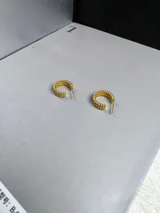 Detail view of triple-layered braided gold C-hoop earrings on a fashion book background