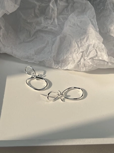 Macro detail of minimalist silver knotted earrings on a textured white background