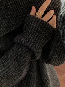 Close-up of golden wavy curve ring on hand with dark grey knit sweater background