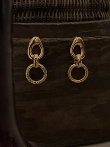 Detail of gold geometric drop earrings with twisted texture on rustic wood background