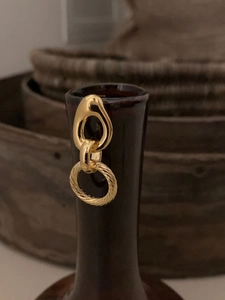 Detail of interlocking gold geometric earrings with spiral texture on a vintage ceramic vase