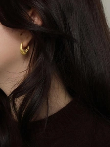 Gros plan d'une boucle d'oreille anneau S925 dorée avec texture brossée sur le lobe