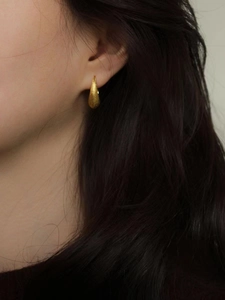 Boucles d'oreilles goutte dorées avec finition mate, portées par un mannequin de profil