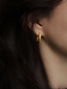 Gros plan d'une boucle d'oreille goutte dorée à texture métallique brossée sur mannequin