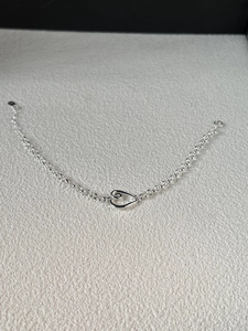 Detailed close-up of a silver rolo chain bracelet with a hollow heart pendant and spring clasp