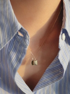 Detail of a gold double pendant necklace with oval and rectangular charms on a striped shirt