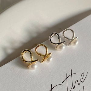 Close-up of gold and silver knot earrings with pearls on a minimalist white card