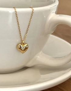 Détail du pendentif cœur en argent 925 doré avec zircons sur le bord d'une tasse blanche