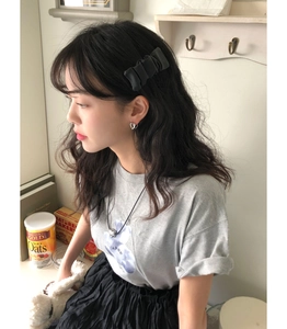 Close-up of hollow silver heart stud earrings paired with a black bow hair accessory