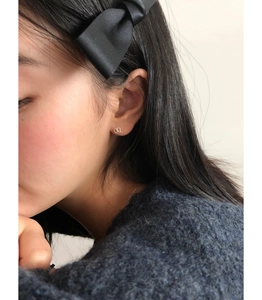 Close-up of small golden hollow heart stud earrings worn by a model in soft lighting