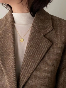 Close-up of golden heart pendant necklace with pleated texture on a woman in a brown blazer