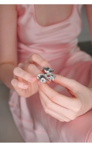Close-up of silver bow ring with textured finish on model fingers and pink silk background