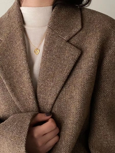 Close-up of golden pleated heart pendant with a central zircon on a model wearing tweed