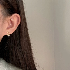 Detail of cross knot gold stud earring with natural pearl on model's ear earlobe