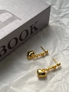 Close-up of gold heart drop earrings featuring Love lettering and arrow details