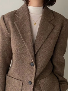Detail of a gold heart pendant necklace styled with a brown tweed blazer and knit top