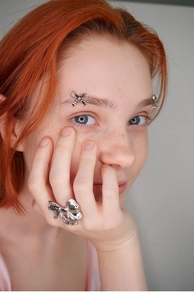 Close-up of a silver bow ring and matching bow eyebrow jewelry on a model