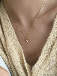 Gros plan d'un collier doré minimaliste avec pendentif croix à quatre billes sur pull