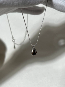 Macro shot of silver teardrop pendant with mirror-polished finish on a box chain