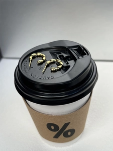 Detail shot of gold C-shaped twisted hoop earrings on a minimalist white coffee cup