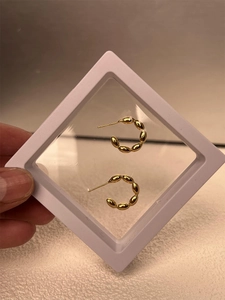 Detail view of a gold-plated beaded C-shape earring in a white suspension display box