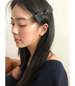 Side view of model wearing a black satin bow hair clip with hollow silver stud earrings