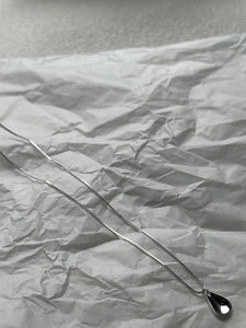 Detailed view of silver necklace with black teardrop pendant on white crumpled paper