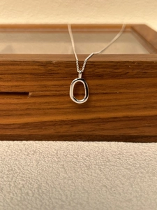 Close-up of a minimalist 925 sterling silver oval pendant necklace on a wooden jewelry box