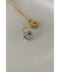 Détail de colliers cadenas cœur argent et or avec gemmes bleues sur un plateau
