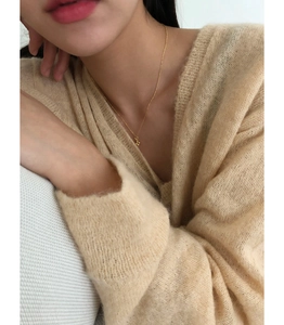 Détail d'un collier croix en argent 925 doré minimaliste sur un pull en maille beige