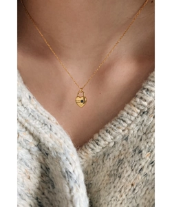 Détail d'un collier cœur doré avec gravure de date et pierre bleue sur pull en maille
