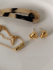 Close-up of golden heart stud earrings with small diamonds and a date-engraved necklace