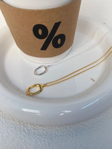 Minimalist silver and gold oval pendant necklaces displayed inside a white ceramic dish