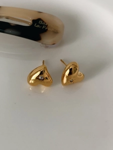 Close-up of golden heart earrings with a central zircon inlay on a white surface