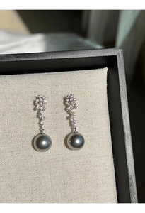Macro detail of dark grey pearl drop earrings with sparkling zircon floral studs in box