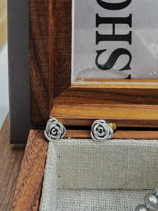 Detailed shot of vintage 925 silver rose stud earrings on a rustic linen jewelry box