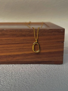 Detail of a minimalist gold necklace with a polished oval open pendant on a wooden case
